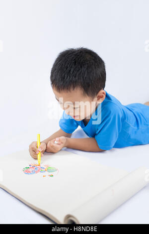 Happy Little Chinese Boy colorazione mentre sdraiato sul pavimento Foto Stock