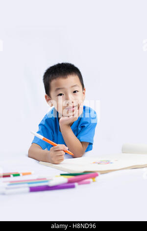 Happy Little Chinese Boy colorazione mentre sdraiato sul pavimento Foto Stock