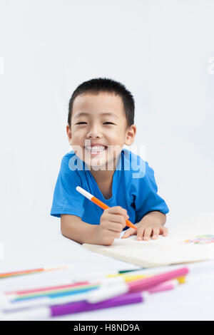 Happy Little Chinese Boy colorazione mentre sdraiato sul pavimento Foto Stock