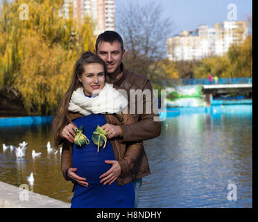 Incinta sorridente giovane con baby bootees nel parco vicino lago. Tempo di autunno Foto Stock