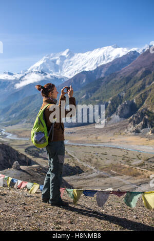 Turista femminile a fotografare il paesaggio sul telefono cellulare durante il circuito di Annapurna trekking in montagna himalayana, Nepal Foto Stock