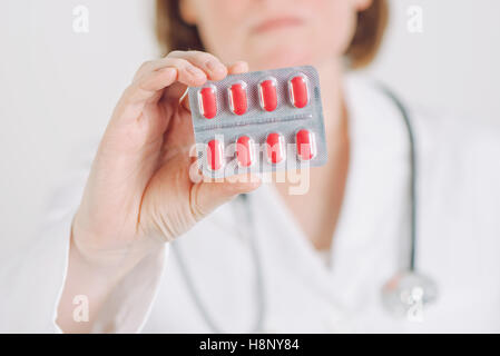 Medico donna offrendo le compresse di colore rosso per il paziente, la sanità e la farmacia concetto, il fuoco selettivo Foto Stock