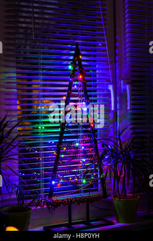 Moderna struttura ad albero di natale luce colorata decorazione presso la finestra Foto Stock