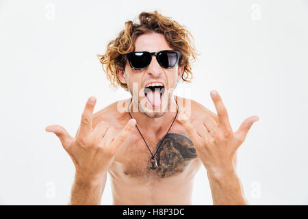 Crazy curly uomo in occhiali da sole che mostra la linguetta e rock gesti con le mani isolati su sfondo bianco Foto Stock
