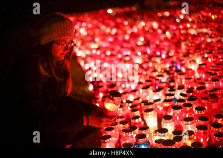 Una vista notturna di una donna tenendo un lampion davanti a un folto gruppo di bruciare lampions sul pavimento al cimitero in Croazia. Foto Stock