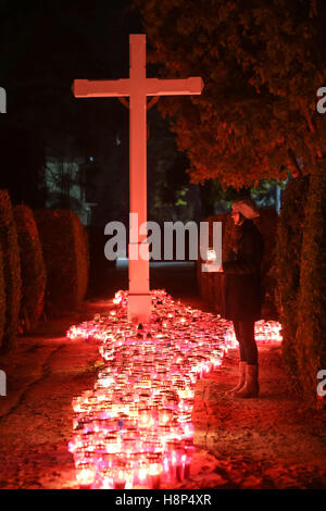 Una vista notturna di una donna tenendo un lampion davanti a un folto gruppo di bruciare lampions sul pavimento al cimitero in Croazia. Foto Stock