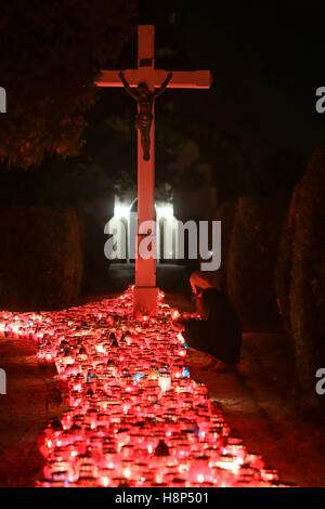 Una vista notturna di una donna tenendo un lampion davanti alla croce al cimitero di Velika Gorica, Croazia. Foto Stock