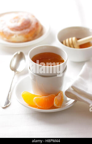 Tangerine inceppamento in una ciotola con le fette di frutta, miele e pasticceria su un tavolo per la colazione. Foto Stock