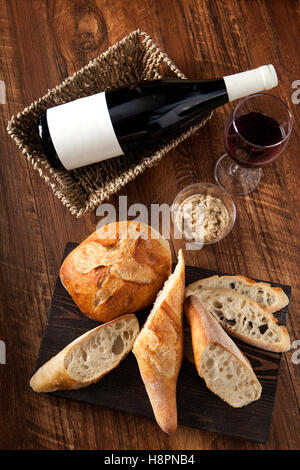 Baguette e la pagnotta di pane con vino rosso sul tavolo di legno Foto Stock