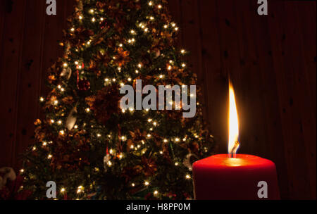 Singola candela rossa nella parte anteriore di un albero di Natale con luci bianche Foto Stock