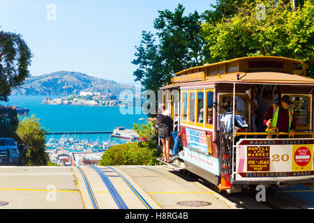 Un cavo auto piena di turisti in corrispondenza del picco di Hyde Street andando oltre il bordo verso il punto di vista della isola di Alcatraz nella baia di SF Foto Stock