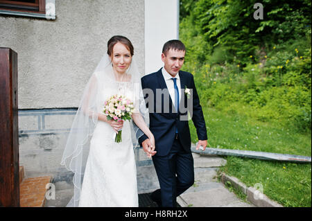 Coppie in viaggio di nozze a piedi giù per le scale per chiesa tenendo le mani Foto Stock