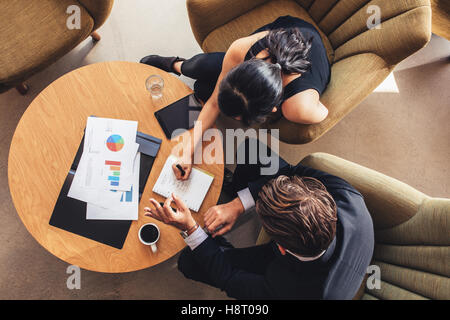 Vista dall'alto di due uomini di affari che i lavori di pianificazione intorno al tavolo. Imprenditore e la donna passando attraverso la Lista da fare mentre sitt Foto Stock