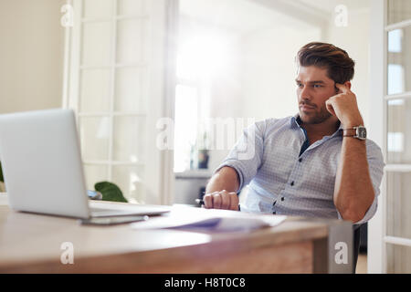 Colpo di imprenditore seduta a tavola guardando laptop e pensare. Considerato imprenditore lavora da casa in ufficio. Foto Stock