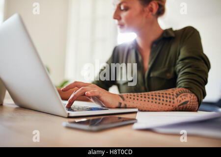 Colpo di donna che lavorano sul portatile a casa. Donna seduta a tavola con le mani sulla tastiera del notebook. Foto Stock
