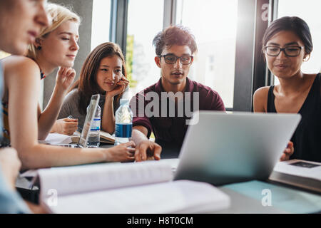 amici universitari socializzano e studiano insieme per un esame in biblioteca. Gruppo di studenti seduti a un tavolo in biblioteca e usini Foto Stock