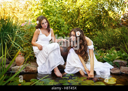 Due sorelle in vestiti bianchi presso il laghetto di ninfee. Le donne attingere acqua nella piccola brocca di argilla. Foto Stock