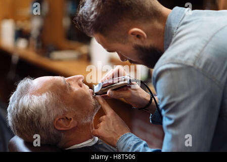 Vista laterale del giovane barbiere barba di fresatura Foto Stock