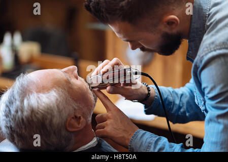 Vista laterale del giovane barbiere barba di fresatura Foto Stock