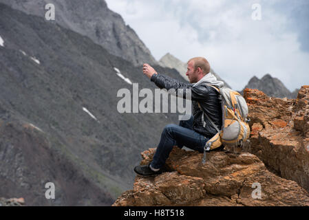 Turistico con uno zaino seduti sulla cima della montagna e fotografare il telefono. L'altezza di 3000 metri. Foto Stock