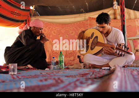 I beduini a suonare la chitarra e il fumo in tenda, valle di Wadi Rum, deserto in Giordania Foto Stock