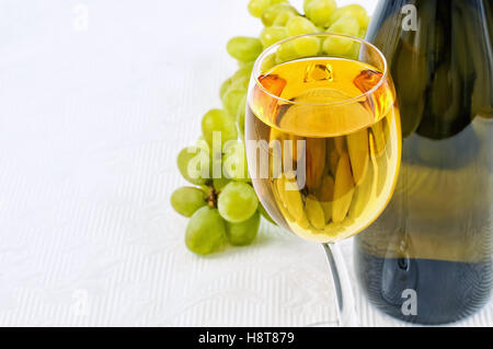 Winglass,bottiglia e uva verde sulla tovaglia bianca closeup immagine Foto Stock