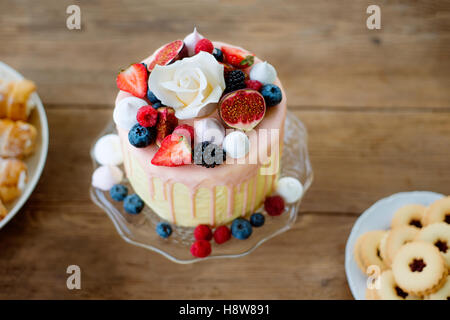 Torta con vari frutti di bosco, meringhe e rose su cakestand. Foto Stock