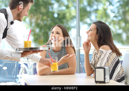 Felice informale riunione amici in un bar con una finestra con verde all'aperto in background e il cameriere che serve rinfreschi Foto Stock