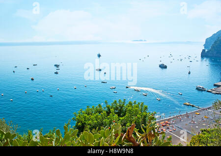 La vista dalla pendenza sulla costa, accogliente spiaggia, numerosi yacht e barche nel porto di Marina Grande Porto, lussureggiante vegetazione del giardino locale Foto Stock