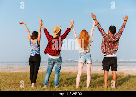 Vista posteriore di un gruppo di giovani amici stando in piedi e tenendo le mani alzate in esterno Foto Stock