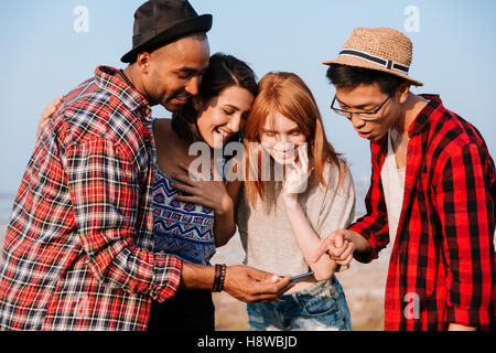 Gruppo di sorridere i giovani e permanente utilizza lo smartphone insieme Foto Stock