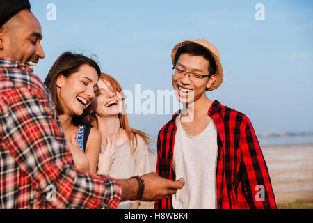 Gruppo multietnico di allegro giovani amici in piedi e ridere insieme all'aperto Foto Stock
