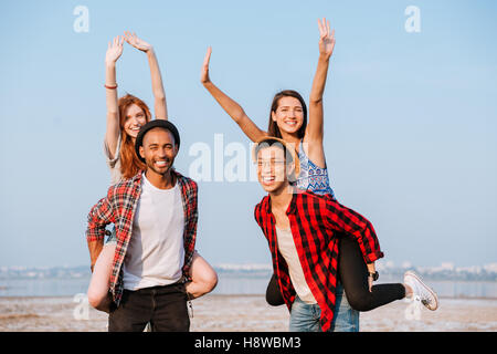 Due allegro giovani uomini permanente e la holding fidanzate sulle loro spalle all'aperto Foto Stock