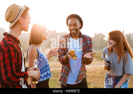 Gruppo multietnico di allegro giovani con birra e soda parlando e ridendo all'aperto Foto Stock