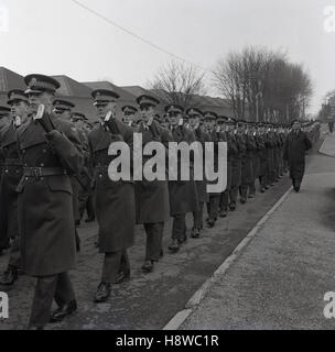 Anni sessanta, storici grandi line-up o formazione di uniformata regimental soldati con fucili a canna rigata marciando in unisono in un accampamento militare o di base. Foto Stock