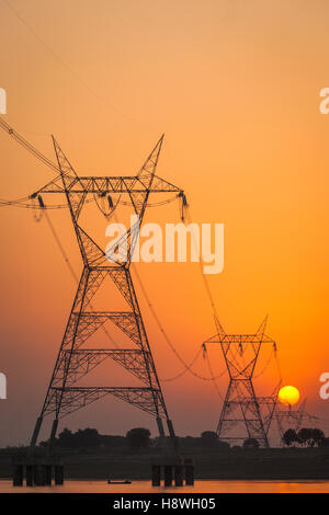 Tralicci di elettricità nella foto contro un sole che sorge sul fiume Gange, India Foto Stock