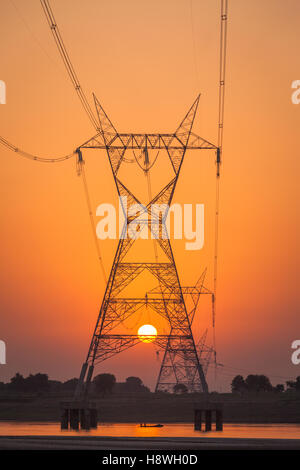 Tralicci di elettricità nella foto contro un sole che sorge sul fiume Gange, India Foto Stock