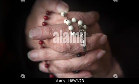 Vecchio mani femminili pregando e tenendo un rosario Foto Stock