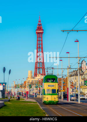 Tradizionali di tram che corre lungo la passeggiata sul lungomare con torre in background, Blackpool, Lancashire, Regno Unito. Foto Stock