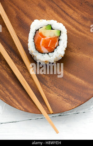 Unico uramaki sushi roll con salmone fresco e avocado in alghe e riso servito su una tavola di legno plater con bacchette Foto Stock