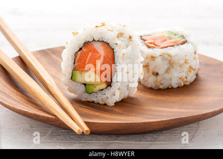Due salmone fresco e avocado uramaki sushi servita su un piatto di legno con uno in posizione verticale per mostrare gli ingredienti Foto Stock