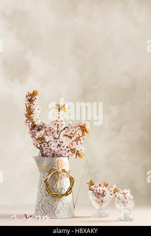 Primavera sbocciano i fiori in caraffa con riempito gli occhiali antichi sul tavolo di legno Foto Stock