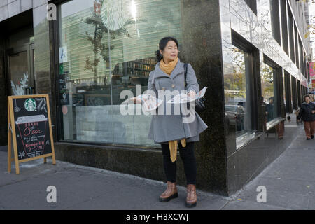 Una donna cinese distribuendo volantini fuori Starbucks su Main Street a Chinatown, lavaggio, Queens, a New York City Foto Stock