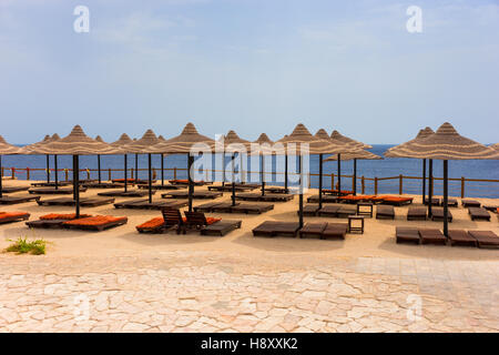 Paesaggio di spiaggia con lettini in legno, ombrelloni di paglia e limpido mare blu Foto Stock