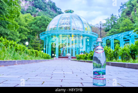 Bottiglia in vetro di Borjomi acqua minerale con la fonte naturale di acqua sotto il padiglione sullo sfondo Foto Stock