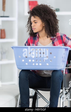 Una donna su una sedia a rotelle carring un cestello a fare il bucato Foto Stock