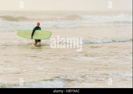 Surfer lasciando l'acqua dopo un sunrise 'dawn patrol' sessione di surf in spiaggia di Jacksonville, Florida, Stati Uniti d'America.