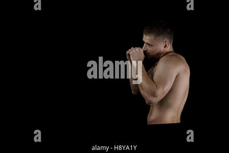 La formazione di giovani boxer muscolare su uno sfondo nero. Punzoni praticato prima della lotta. Luce dura, illuminazione scuro Foto Stock