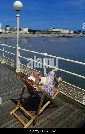 Una donna matura la lettura in una sedia a sdraio su Worthing Pier. West Sussex. In Inghilterra. Regno Unito Foto Stock