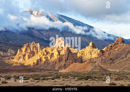 Rocky Mountain tops incandescente nella luce del tramonto ai piedi del vulcano El Teide coperto di nuvole basse in Tenerife parco nazionale Foto Stock